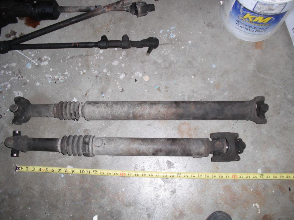two driveshafts laid out on concrete floor with tape measure