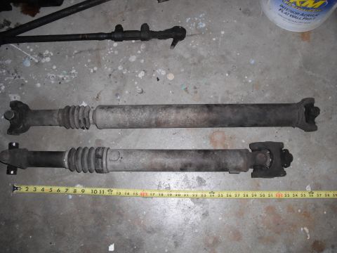 1991 Ford Bronco - Two drive shafts and a steering linkage component are shown on a concrete floor, measured with a tape measure.