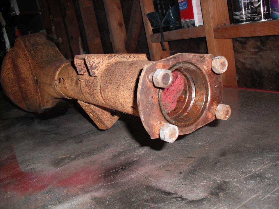 Rusty axle housing with differential bowl and four-stud hub flange on garage floor