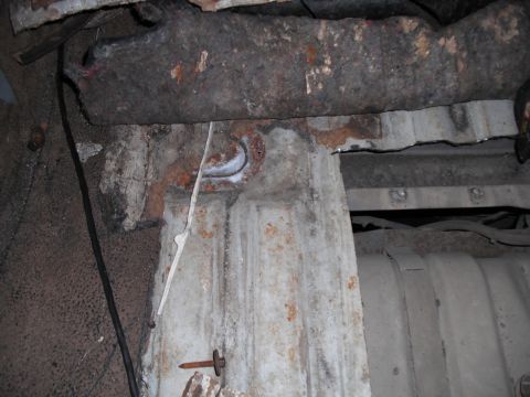 1991 Ford Bronco - Close-up view of the corroded undercarriage of a vehicle, showing a fuel tank and supporting structures.