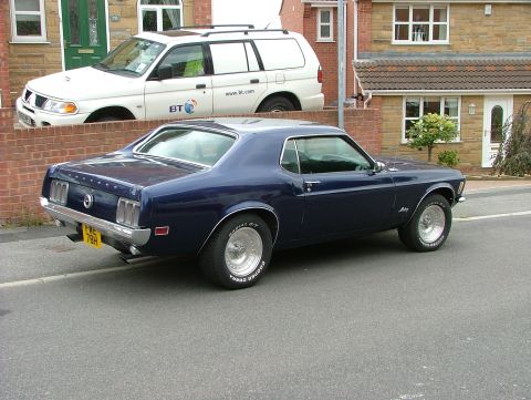 1970 Ford Mustang - Dark blue 1970 Ford Mustang seen from the rear, with a white SUV in the background.