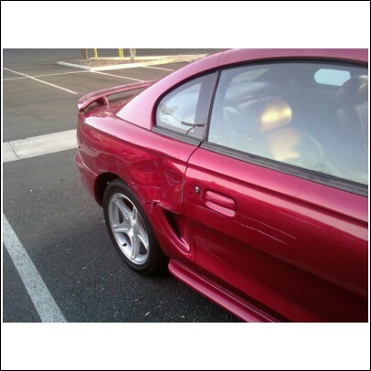 Red coupe with significant body damage on the rear quarter panel and door, showing scratches and a dent
