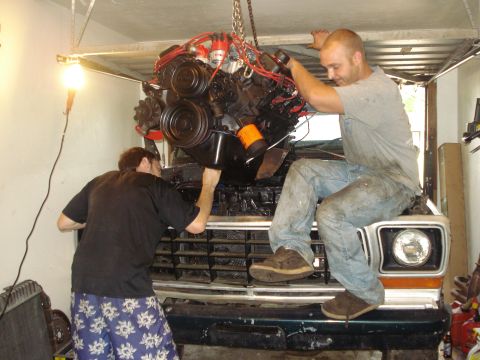 1978 Ford Bronco - An engine is being lowered into place in a vehicle's engine bay by two mechanics.