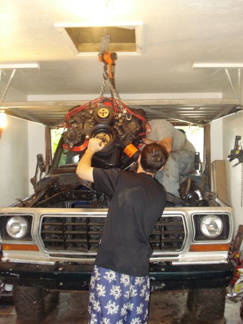 1978 Ford Bronco - Mechanics work on an engine being lifted into a 1978 Ford Bronco in a garage.