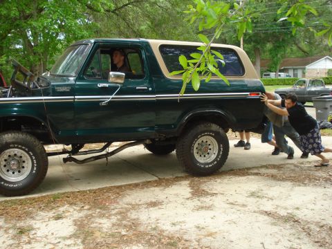 1978 Ford Bronco - A group of men push a green 1978 Ford Bronco from the side.