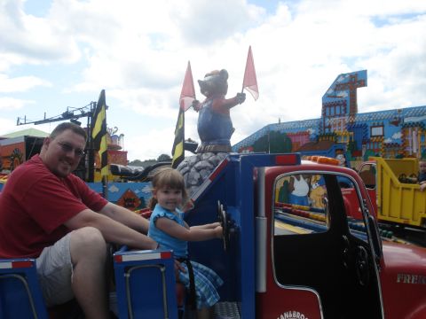 2000 Ford Crown Victoria - A father and daughter enjoy a ride on a toy truck at an amusement park with other rides in the background.