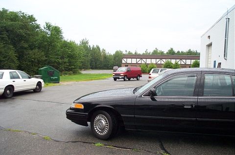2001 Ford Crown Victoria - A black sedan is in the foreground with other vehicles and a building in the background.