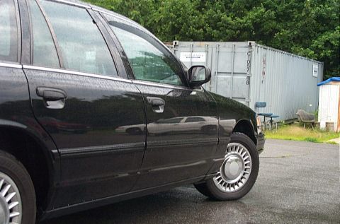 2001 Ford Crown Victoria - A black 2001 Ford Crown Victoria is parked on a wet surface, with a large shipping container in the background.