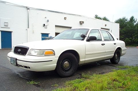 2001 Ford Crown Victoria - A white 2001 Ford Crown Victoria sedan is parked in front of a white building.