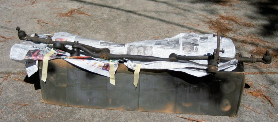 Steering linkage components laid out on newspaper and a dark container
