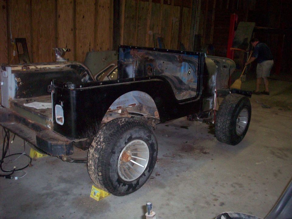 Black Jeep CJ-series body on jack stands, missing doors and windshield, in a workshop
