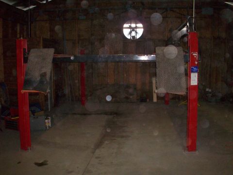 1978 Jeep CJ5 - A two-post car lift stands ready in a workshop, with a circular window visible in the background.