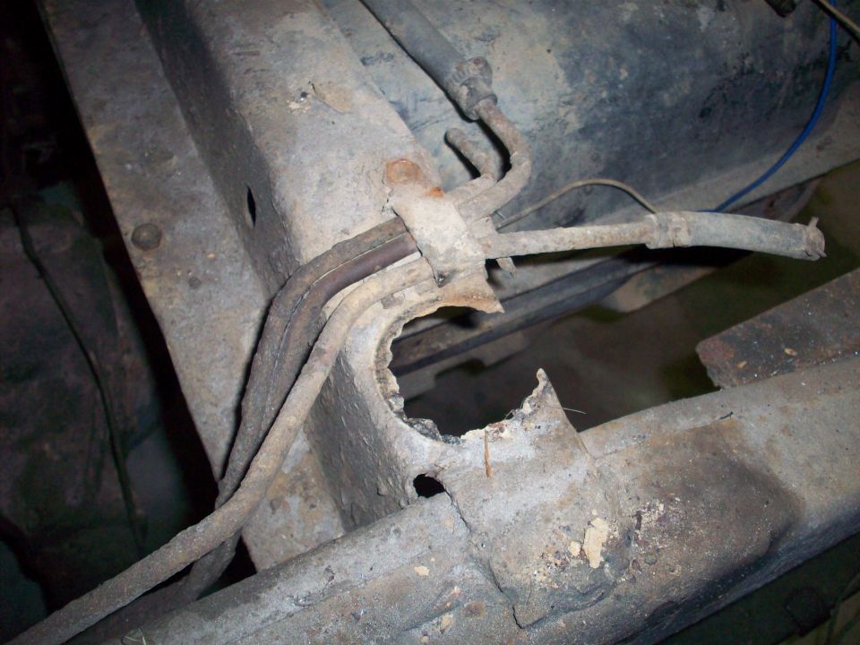 Close-up of a heavily rusted vehicle frame with fuel lines and a hole in the metal