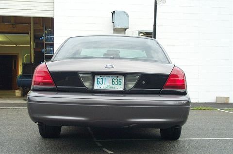 2001 Ford Crown Victoria - The rear of a Ford Crown Victoria is parked in front of a white building with the garage door open.