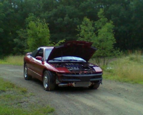 1993 Ford Probe - Red 1993 Ford Probe with its hood open, sitting on a dirt road with trees in the background.