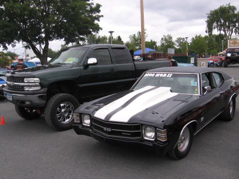 2001 Chevrolet Silverado 1500 - A classic black muscle car with white racing stripes is parked next to a lifted green pickup truck.
