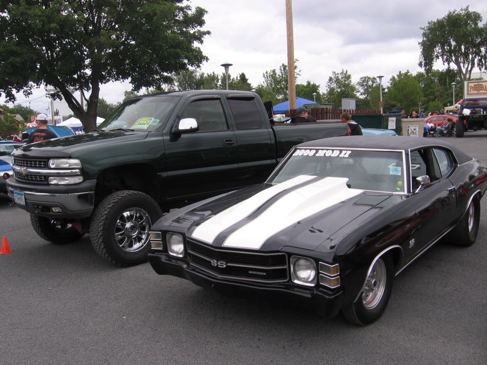Black muscle car with white stripes and a lifted green pickup truck parked side-by-side