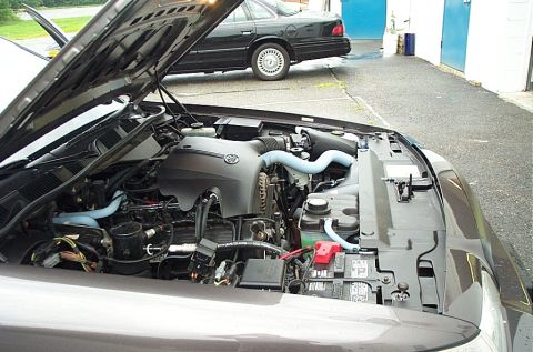 2001 Ford Crown Victoria - The engine bay of a car is open, with another car parked in the background.