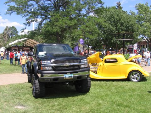 2001 Chevrolet Silverado 1500 - A black pickup truck and a yellow hot rod are displayed on a grassy field with people in the background.