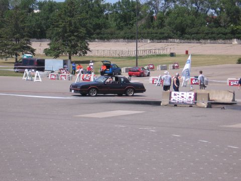 2001 Chevrolet Silverado 1500 - A black coupe with an orange stripe drives on a track with other vehicles and spectators present.