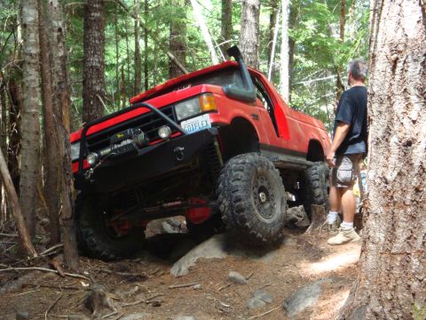 1978 Ford Bronco - Modified red SUV navigates a challenging off-road course through a forest.