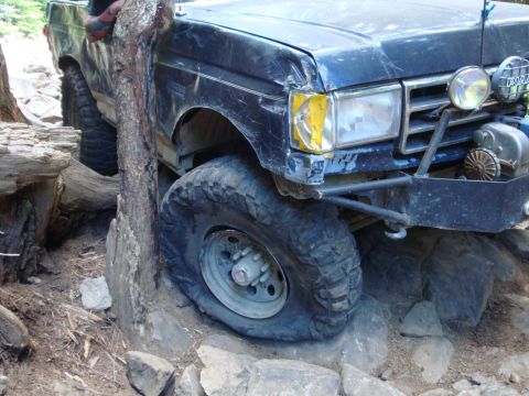 1978 Ford Bronco - This dark blue SUV, likely from the early 1980s, is shown navigating a rocky trail with its front quarter visible.