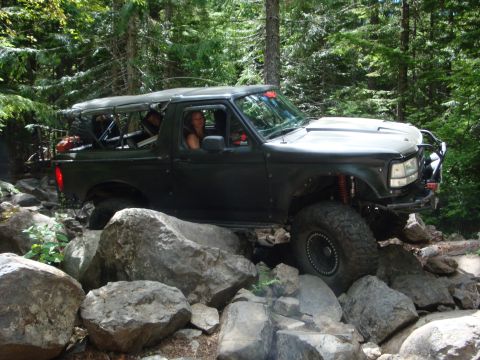 1978 Ford Bronco - A dark green Ford Bronco navigates a challenging rocky trail in a wooded area.