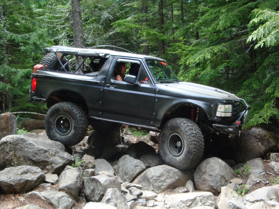 Modified dark gray Ford Bronco with large tires navigating a rocky trail