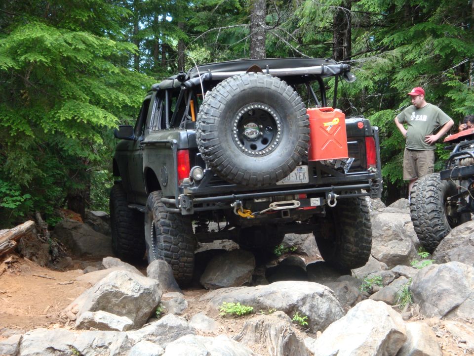 Black 1978 Ford Bronco with spare tire and gas can on rear, navigating rocky terrain
