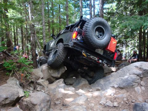 1978 Ford Bronco - A modified off-road vehicle attempts to climb over large rocks on a wooded trail.