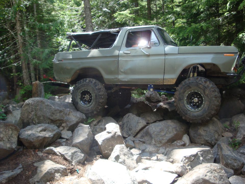 Modified Bronco climbing over large rocks on a trail