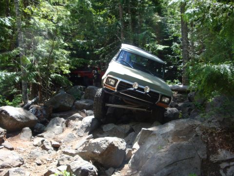 1978 Ford Bronco - Two off-road vehicles tackle a challenging rocky path through a dense forest.
