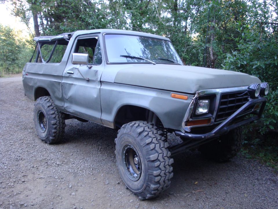 Green lifted late-1970s Ford Bronco with soft top and mud tires on gravel