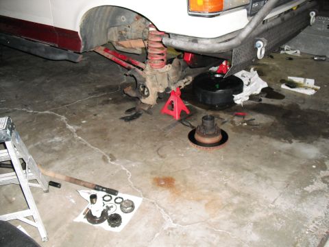 1991 Ford Bronco - Front suspension and brake components of a 1991 Ford Bronco are disassembled on a garage floor.