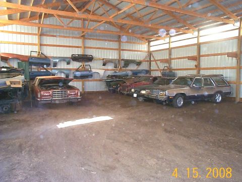 1984 Ford Mustang - A collection of vehicles and automotive parts are stored inside a barn.