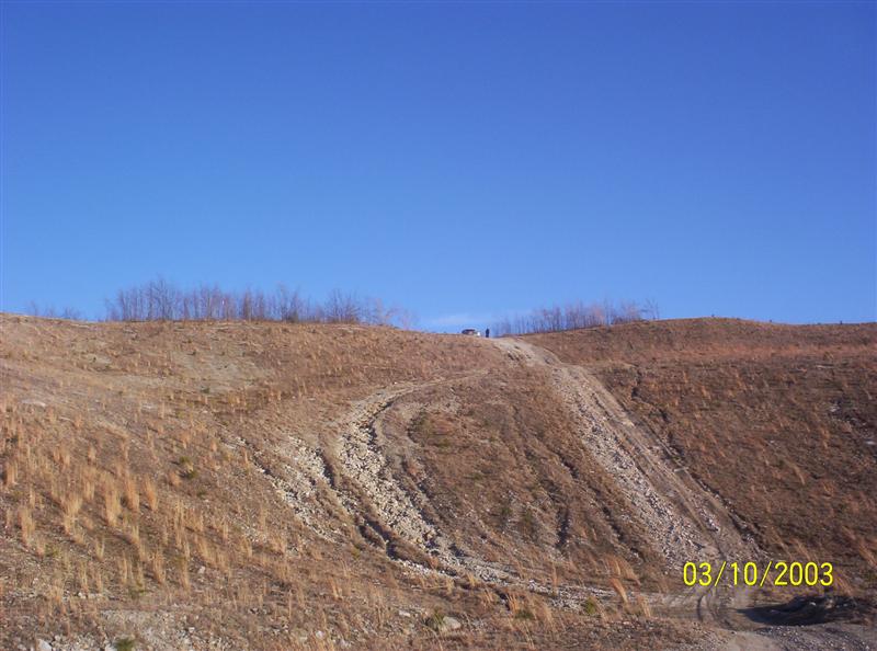 Barren brown strip-mine hillside with faint dirt tracks, blue sky, dated 03/10/2003