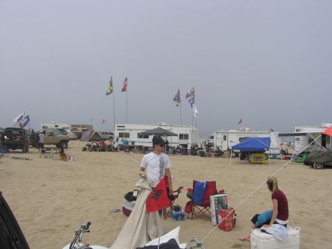 1989 Ford Bronco - A beach campsite scene with multiple RVs, ATVs, and people gathered on the sand.
