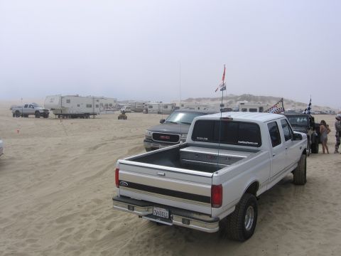 1989 Ford Bronco - Several vehicles and RVs are parked on a sandy beach under a hazy sky.