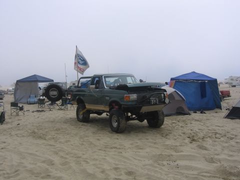 1989 Ford Bronco - 1989 Ford Bronco with modifications parked on a sandy beach with tents and other vehicles in the background.