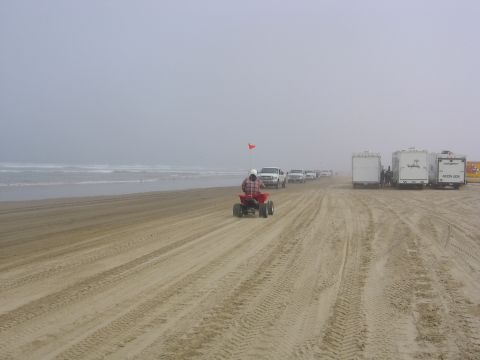 1989 Ford Bronco - A person rides an ATV on a foggy beach, with a line of trucks and trailers parked nearby.
