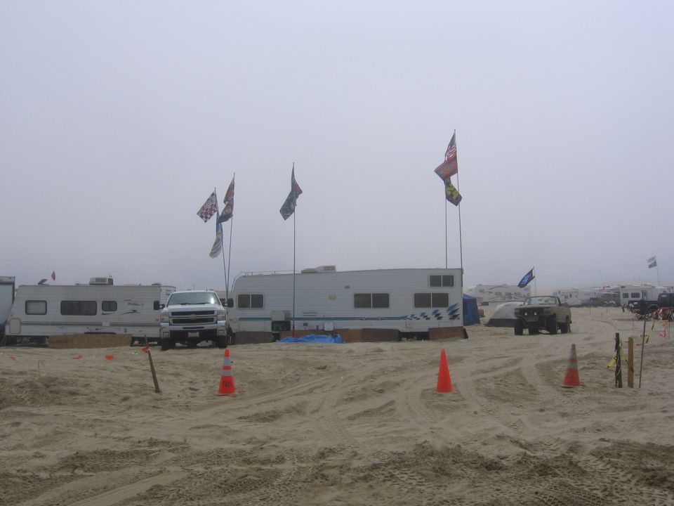 White pickup truck parked on a sandy beach with RVs and flags