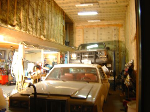 1984 Ford Mustang - A white sedan is parked in a garage, with a lifted truck positioned above it.