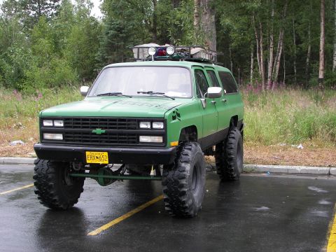 1990 Chevrolet Suburban - A modified 1990 Chevrolet Suburban sits parked on a wet asphalt lot.