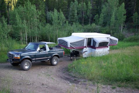 1995 Ford Bronco - 1995 Ford Bronco is seen towing a pop-up camper in a wooded area.