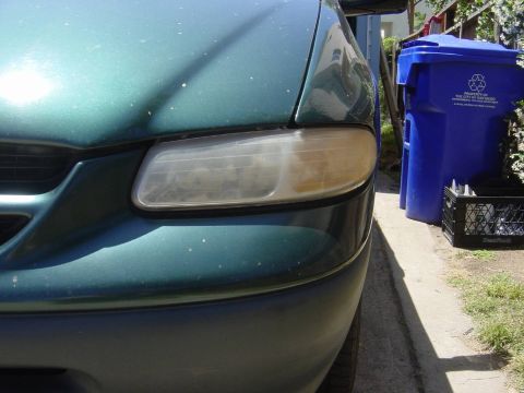 1995 Ford Taurus - The front passenger side of a green 1995 Ford Taurus is visible, parked next to blue recycling bins.