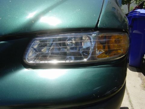 1995 Ford Taurus - Close-up of the front headlight and bumper of a green 1995 Ford Taurus, showing some wear and tear.