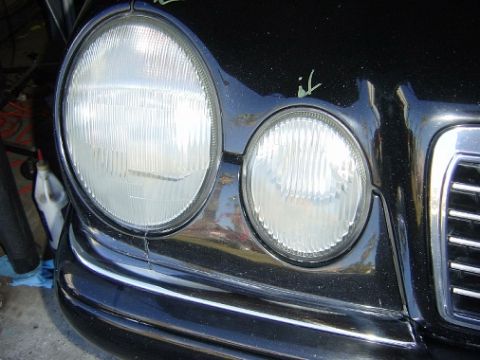 1995 Ford Taurus - The front passenger side headlight assembly of a black Mercedes-Benz E-Class is shown in this close-up view.