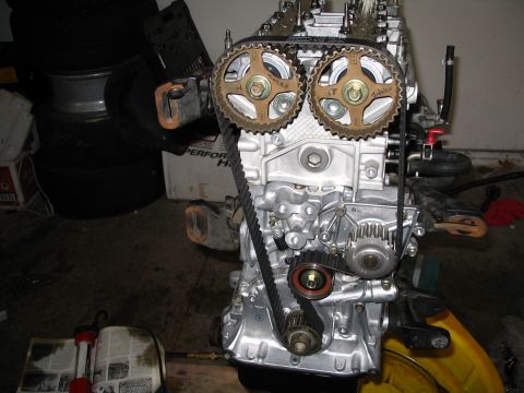 1994 Acura Integra - Close-up of an engine's timing belt and gears, with various automotive parts and tires visible in the background.