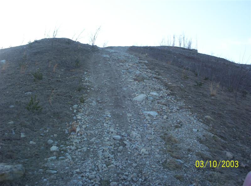 Steep rocky off-road trail up a sparse hillside, dated 03/10/2003; no vehicle visible