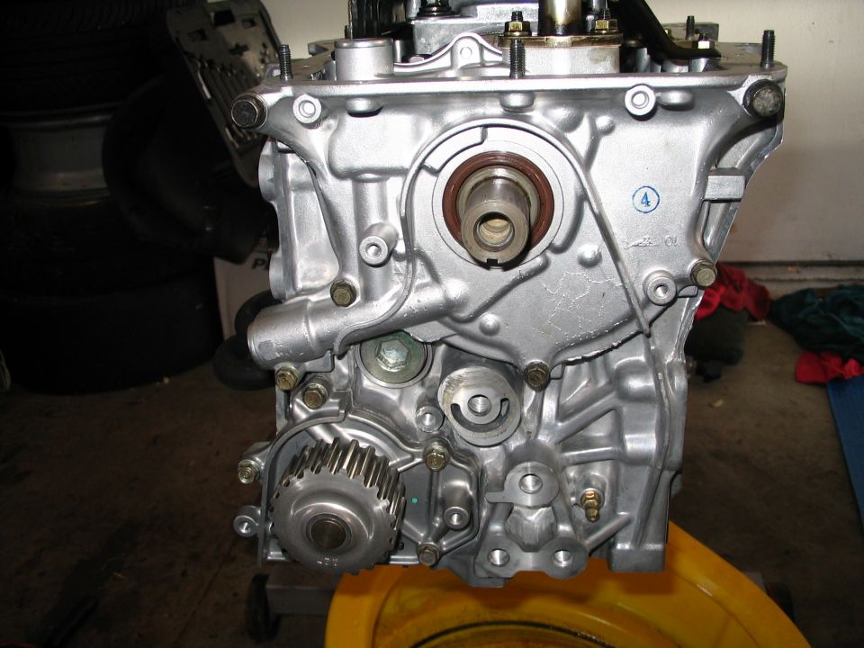 Timing side of a clean aluminum four-cylinder engine on a stand with belt removed and crank sprocket exposed